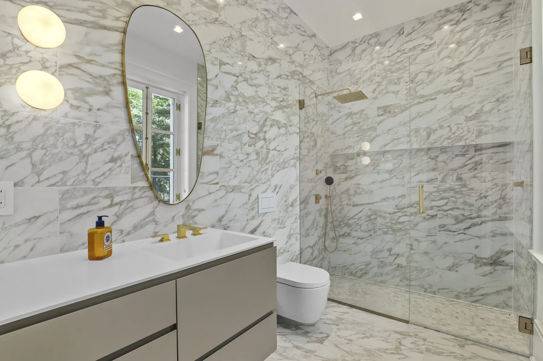 A marble bath with brass fixtures and a frameless glass shower
